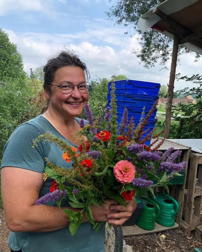 Fleurs à couper fraîches et écologiques et abonnnements floraux, produits sur la ferme florale Bluëtte Farming Maraîchage et fleurs à Bruxelles Anderlecht ; portrait d'une participante heureuse d'un atelier floral avec des bouquets de fleurs