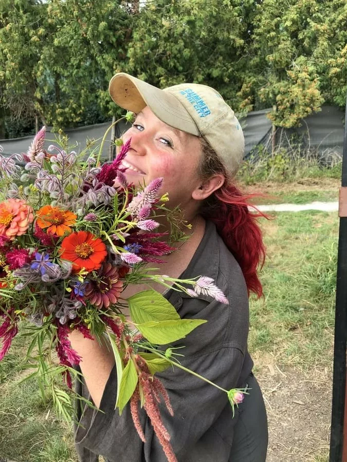 Fleurs à couper fraîches et écologiques et abonnnements floraux, produits sur la ferme florale Bluëtte Farming Maraîchage et fleurs à Bruxelles Anderlecht ; portrait d'une cliente heureuse avec un bouquet à base de zinnias et célosia