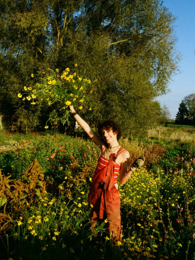 Cliente heureuse de la ferme florale Bluëtte Maraîchage et fleurs à Anderlecht, tenant un bouquet de fleurs des champs, de la tagète orange, dans sa main